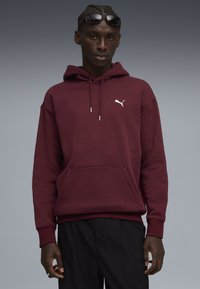 Bordová mikina s kapucňou a klokaniou vreckom, so sivým logom Puma na hrudi. Texturovaná tkanina a ribbované manžety.