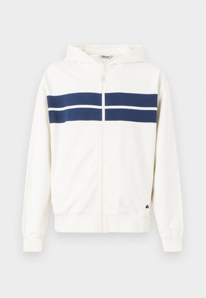 Hvit hettejakke med marineblå horisontale striper over brystet og på ermene. Har en hette og ribbestrikkede mansjetter ved håndleddene.