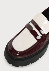 Λούστρο loafers με παχιά μαύρη σόλα, λευκό επάνω μέρος και σκούρα βουργουνδί διακόσμηση και λωρίδα μπροστά.