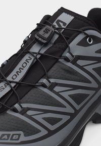 Κοντινή εικόνα μαύρου και γκρι παπουτσιού πεζοπορίας Salomon με σύστημα γρήγορου δέσιματος και γεωμετρικά σχέδια στα πλευρά.