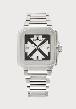 Montre carrée en métal argenté avec un motif de croix noir et blanc sur le cadran, aiguilles argentées, affichage de la date et bracelet à maillons.