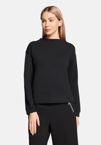 Sweat-shirt noir à col rond avec manches longues, en tissu lisse. Présente une coupe décontractée et des accents décoratifs subtils à l'ourlet.
