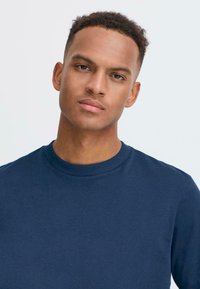 Tengerész navy crewneck pulóver, puha anyagból készült, bordás nyakkal és beültetett ujjal, sima textúrával és minimális dizájnnal.