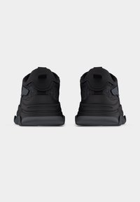 Paire de baskets de sport noires et gris foncé vues de dos sur un fond uni gris clair.