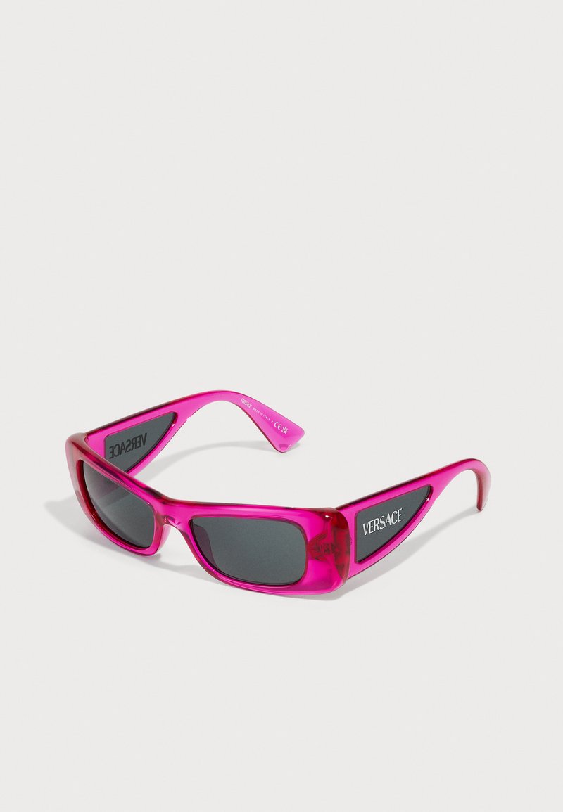 Gafas de sol transparentes en color rosa con lentes oscuros. Forma rectangular, marco grueso y logotipo en las varillas. Diseño elegante y acabado brillante.