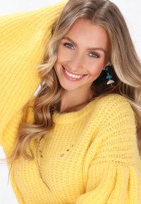 Gelbes Strickpullover mit strukturiertem Rippdesign, lockeren Ärmeln und weitem Ausschnitt. Accessoires mit bunten Statement-Ohrringen.