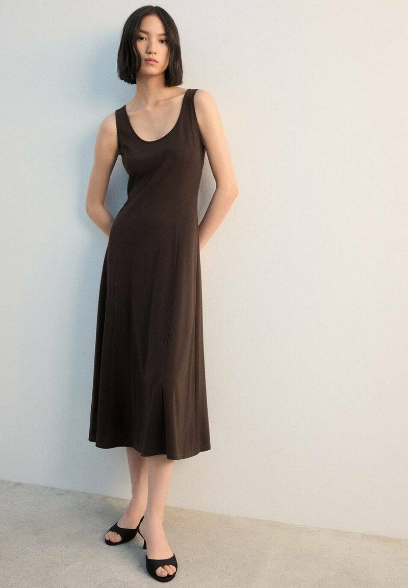Bruine mouwloze maxi-jurk met een ronde hals, een aansluitend silhouet en een lange, vloeiende rok. Gecombineerd met zwarte open-toe hakken.