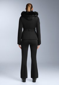 Černá lyžařská bunda s kapucí z umělé kožešiny, přiléhavý střih a páskový pas. Kombinováno s elegantními černými lyžařskými kalhotami se zipem. Hladká textilie po celé délce.