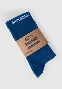 Siniset ribattuja sukkia, joissa valkoinen "SMILODOX" -logo ylhäällä, pakattu ruskealla kartonkibandilla, jossa on koko- ja tuotemerkintätiedot.