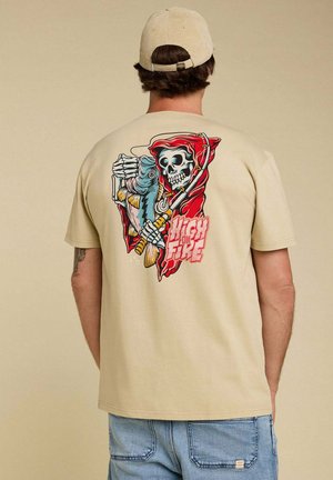 T-shirt en coton beige avec un graphique coloré au dos représentant un crâne tenant un poisson, avec le texte "High on Fire" en dessous.