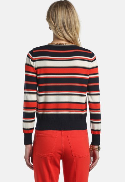 Pull rayé comprenant des couleurs rouge, marine et crème avec des poignets et un ourlet côtelés. Porté avec un pantalon rouge, montrant un col arrondi et un tissu léger.