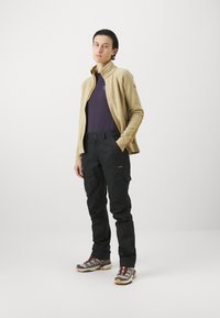 Bežs ar rāvējslēdzēju frotē jaka virs purpursarkanas krekla, apvienota ar melniem kravas biksēm un pelēkām pārgājienu apaviem ar bordo akcentiem.