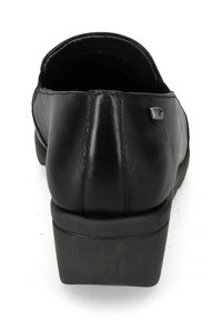 Scarpa in pelle nera con punta arrotondata, tacco basso a blocco, superficie texture, e un piccolo accento metallico vicino al tallone. Vista posteriore.