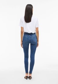 Jeans de denim azul de cintura alta con un ajuste skinny, que cuentan con bolsillos traseros y una textura suave. Combinados con una camiseta blanca básica y tacones.