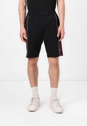 Sorte treningshorts med hvite sidestykker og en rød aksent til venstre. Laget av et mykt materiale, med elastisk midjebånd.