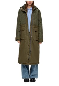 Olijfgroene gewatteerde lange jas met een capuchon, voorzien van een ritsluiting, drukknoopsluiting en twee voorzakken. Draag het over een blauwe hoodie en wijde jeans.
