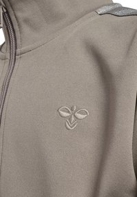 Jasnoszara kurtka na zamek z gładką fakturą, z haftowanym logo liścia na piersi i odblaskowymi akcentami na ramionach.