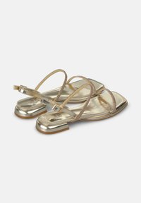 Sandali metallici dorati con sottili cinturini incrociati, punta quadrata, tacco basso e accenti testurizzati sulla cinghia. Design leggero.
