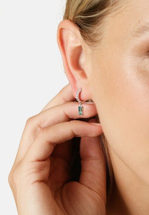 Silberne Creolenohrringe mit einem kleinen türkisfarbenen rechteckigen Stein und funkelnden Akzenten, die direkt unter dem Ohrläppchen hängen.