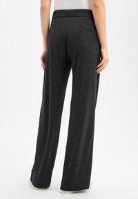 Weit geschnittene Hosen aus dunkelgrauem Stoff mit hohem Bund. Glatte Textur mit dezenten vertikalen Nähten, geeignet für legere Kleidung.