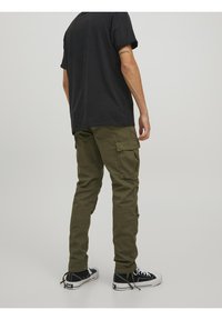 Oliwkowe spodnie bojówki z wieloma kieszeniami, prostym krojem nogawek i lekko teksturowaną tkaniną. Noszone z czarnym t-shirtem i czarnymi trampkami.