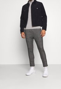 Granatowa sztruksowa kurtka, szara koszulka z półgolfem, szare spodnie w kratę i białe sneakersy. Posiada dwie kieszenie na piersi oraz minimalistyczny design.