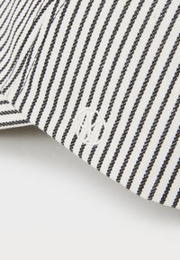 Striped fabric cap in black and white, featuring a textured weave and an embroidered logo in white, positioned on a light background.
