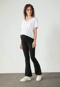 T-shirt branca de mangas curtas com decote em V combinada com calças pretas largas, complementada por sapatilhas brancas. Textura do tecido suave, design casual.