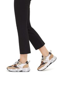 Sneaker con una combinazione di materiali in suede e rete marrone, bianco e nero. Suola bianca spessa con dettagli grafici e una linguetta sul tallone.