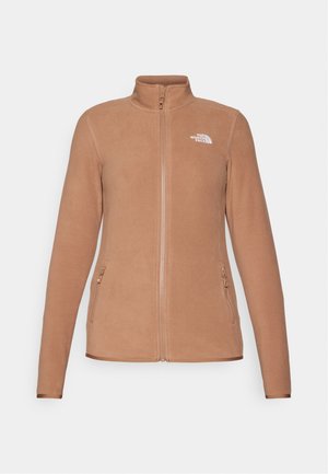 Fleecejakke i beige, med høyt krage, full glidelås og to glidelåslommer på sidene. Merke på venstre bryst. Jevn tekstur.