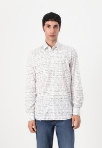 Hvit skjorte med knappelukking som har et gjentagende mønster av håndskrevet svart tekst, lange ermer og normal krage. Kombinert med blå jeans.