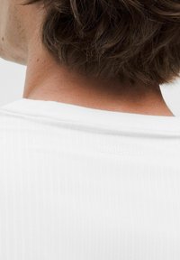 Camisa blanca de manga corta hecha de un material texturizado, con un sutil logotipo en relieve de "lululemon" en la parte posterior.