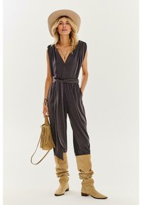 Sivý overal s hlbokým výstrihom do V, zúženým pásom a širokými nohavicami. Skombinovaný s béžovými voľnými čižmami a zodpovedajúcou širokou klobúkom.