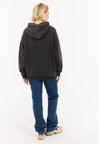 Oversized donkergrijze hoodie met een verstelbare trekkoordkap, ribbelmanchetten en een voorke pocket, gecombineerd met blauwe denim jeans en beige sneakers.