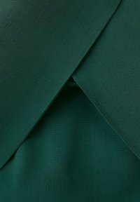 Temno zelena tkanina z zasnovo prekrivajočih se plasti, ki tvorijo V-obliko odprtino na sredini.