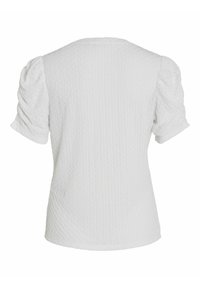 Haut blanc à texture avec des manches courtes bouffantes et un col rond. Présente un motif discret en losanges et un design ajusté.