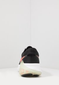 Zapatilla deportiva negra con un upper texturizado, acentos en rosa y una suela translúcida. Presenta un collar acolchado y una tira en el talón para mayor comodidad.