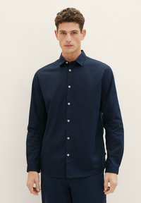 Marineblauwe overhemden met lange mouwen, gemaakt van katoen. Voorzien van een button-down kraag en witte knopen aan de voorkant. Soepele textuur, getailleerde pasvorm.