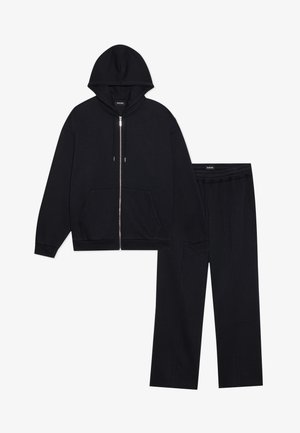 Sudadera negra con cierre de cremallera y bolsillos frontales, combinada con pantalones de chándal a juego que cuentan con una cintura elástica y detalles de costura.