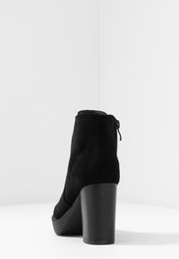 Svart mocka ankelsko med hög blockklack, med dragkedja bak och slät yta. Minimalistisk design utan synliga dekorationer.