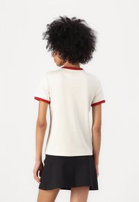 Witte t-shirt met korte mouwen, voorzien van een rode geribbelde kraag en mouwranden, met een aansluitend ontwerp en een zachte textuur. Zwarte rok zichtbaar aan de zoom.