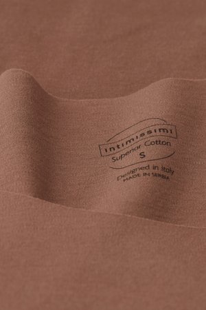 Bomullstyg i varm brun nyans med en mjuk yta. Har en svart tryckt etikett som anger märke, storlek och produktionsdetaljer.