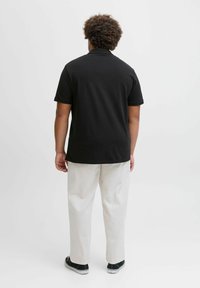 Schwarzes Polo-Shirt mit klassischem Kragen, kombiniert mit hellbeigen Hosen und schwarzen Sneakers. Glattes Material, lockere Passform.