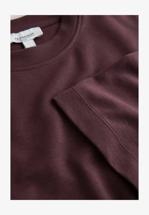 Bordó pamutpóló kerek nyakkivágással, rövid ujjú és látható varrással. Sima textúrájú, hétköznapi kialakítás.