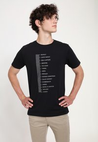 Camiseta de algodón negra con texto blanco que enumera varias descripciones, con un gráfico de regla en el lado izquierdo, diseño de cuello redondo.