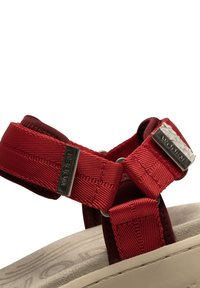 Punat punujaulaksa punjat punjanya dengan kemasan matte, tali yang dapat disesuaikan, dan alas kaki beige bertekstur dengan detail logo timbul.