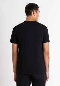 Camiseta negra de manga corta, hecha de una tela suave, con cuello redondo y un corte relajado, sin patrones ni acentos visibles.