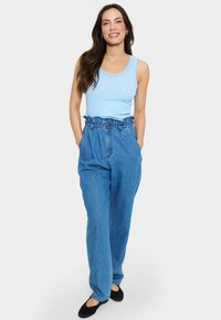 Ljusblå linne med hjärttryck, kombinerat med högmidjade jeans. Byxorna har en rynkad midja och en avslappnad passform. Svarta ballerina.