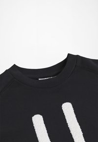 Černá mikina s kulatým výstřihem a silnými bílými vertikálními pruhy z chenille na přední straně, vystavená na bílém pozadí.