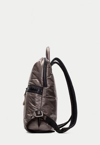 Mochila acolchada gris con cremallera texturizada negra, correas ajustables negras y detalles de logo en la correa. Diseño compacto y aerodinámico.
